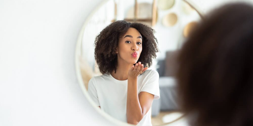 Woman looking at skin in mirror after reading our new year's resolutions for your skin
